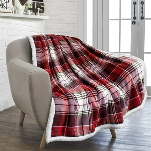 Detail of red and white plaid sherpa blanket draped over a cozy grey armchair