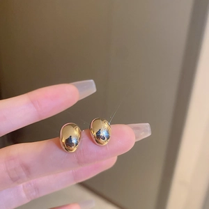Polished gold bean stud earrings shown on finger for size perspective and high shine