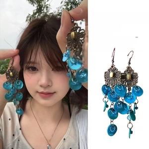 Detailed close-up of retro peacock blue bohemian tassel earrings with bronze floral accents