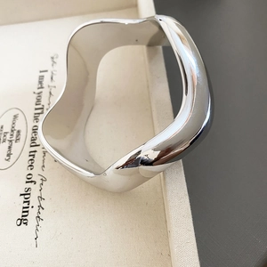Detail of minimalist silver polished wavy bangle with fluid design and modern wide shape