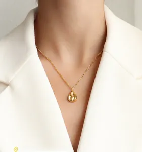 Close-up of a minimalist gold teardrop pendant necklace worn on a white suit model