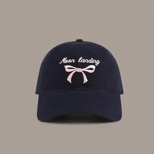 Detail of navy blue baseball cap with pink Moon Landing and bow embroidery