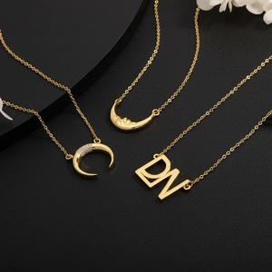 Detailed close-up of 18k gold crescent moon and zircon pendant necklaces on black texture