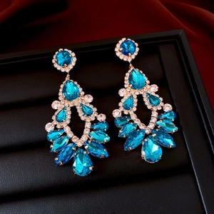 Close-up of golden hollow teardrop earrings with blue crystals on black jewelry box
