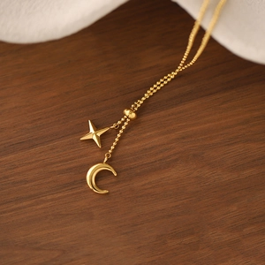 Detail of gold bead chain necklace with star and moon charms on dark wood background