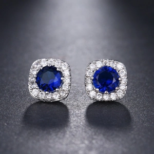 Macro view of silver round stud earrings featuring blue sapphire center stone and zircon halo
