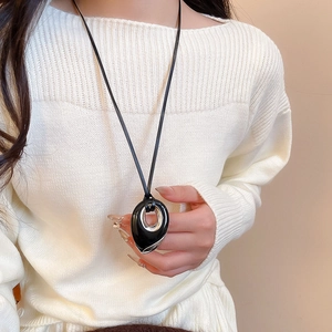 Detail of artistic black teardrop pendant on thin cord worn over a textured white sweater