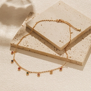 Close-up of gold chain necklace with colorful zircon pendants on stone tiles