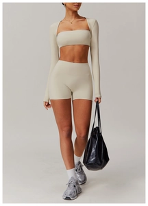 Minimalist beige three-piece yoga set showing long sleeve shrug, sports bra and tight shorts