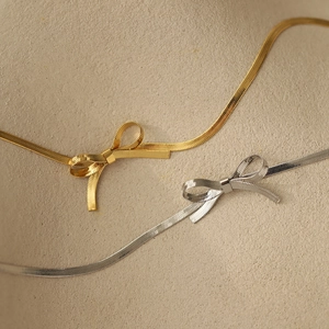 Macro shot of titanium steel bowknot charm necklaces with elegant gold and silver finishes