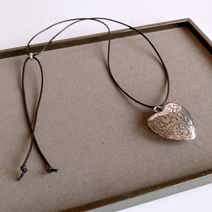 Close-up of engraved silver heart pendant with black wax cord and adjustable beads