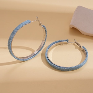 Macro shot of large denim-wrapped silver hoop earrings featuring light blue jean fabric texture