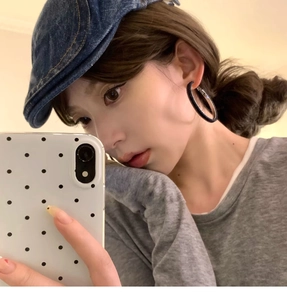 Close-up of black oversized hoop earrings with woven texture and denim newsboy cap accessory