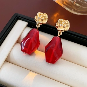 Close-up of elegant gold flower earrings with faceted red pendant on jewelry box
