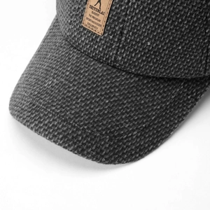 Close-up of deep gray tweed baseball cap with textured fabric and brown leather label