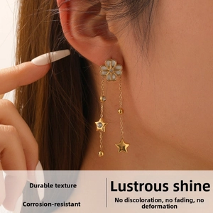 Detailed view of gold tassel earrings with shell flower and crystal star charm on ear