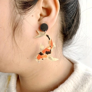 Close-up of asymmetric koi fish acrylic earrings worn by model in orange and black