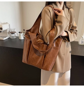 Brown leather large capacity tote bag shown on shoulder in a lifestyle setting