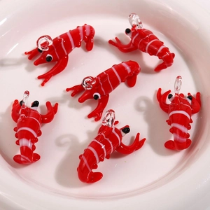 Detail of six handmade glass lobster pendants in a white ceramic bowl for DIY jewelry
