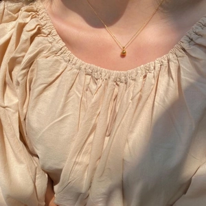Close-up of polished gold teardrop pendant on a fine chain worn by a model