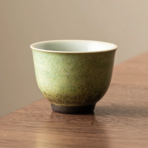 Kiln-baked ceramic tea cup with green gradient glaze on dark wooden tabletop