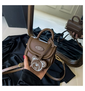 Detail of dark brown leather mini crossbody bag with cute bear charm and logo emblem