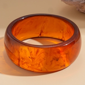 Detail view of thick resin bangle with translucent amber finish and smoky brown patterns