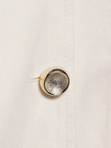 Macro detail of a vintage golden textured button on off-white linen waistcoat fabric