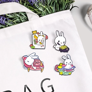Set of four cute white rabbit enamel pins shown pinned on a stylish white canvas bag