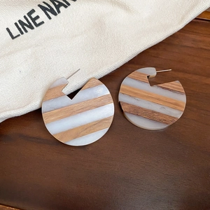 Macro detail of C-shaped wooden and white acrylic striped earrings with silver posts