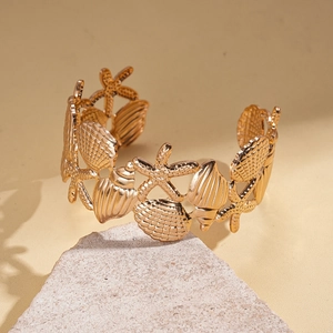 Detail of a golden seashell and starfish open cuff bracelet on a natural stone surface
