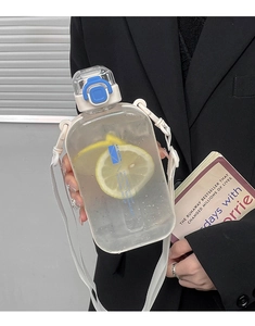 Flat square clear water bottle with blue strap and lemon slices held by hand