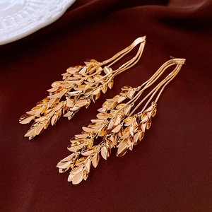 Detail view of golden wheat-ear tassel earrings on a premium dark velvet background