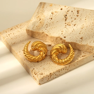 Gros plan sur des boucles d'oreilles spirales dorées texturées sur pierre beige