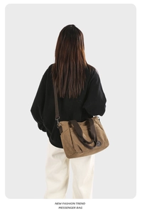 Brown canvas messenger bag with dual handles and long shoulder strap on model