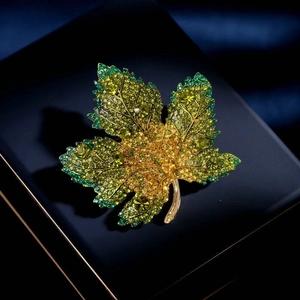 Elegant gold maple leaf brooch with green crystal pavé setting on a blue jewelry box