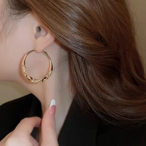 Close-up of model wearing large gold-tone twisted hoop earrings with sparkling rhinestones
