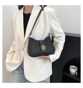 Chic black underarm bag with gold circular lock shown on a model in a white blazer