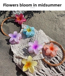 Detailed set of six colorful frangipani flower hair claws resting on a summer beach bag