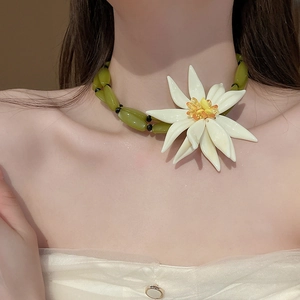 Detail shot of green beaded necklace with large white resin flower pendant for women