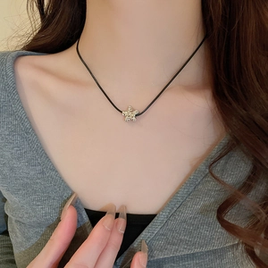 Detailed close-up of a golden star pendant with textured finish on a black cord necklace