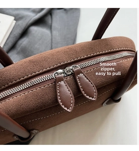 Detail of brown suede handbag featuring silver double zippers and white contrast stitching