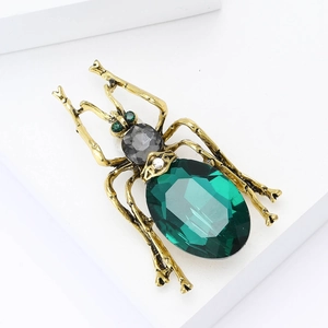 Vintage gold insect brooch featuring large green crystals on white geometric stand