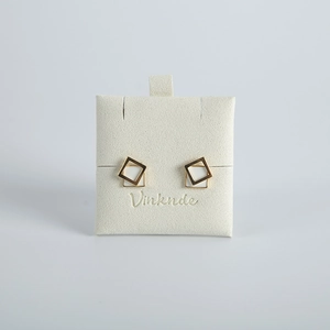 Detail of geometric double square gold stud earrings with white enamel on display card