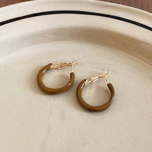 Detailed close-up of C-shaped geometric resin hoop earrings with golden metal clasps