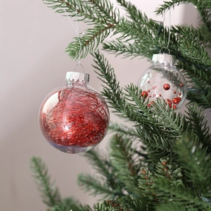 Detail of transparent 6cm Christmas ball with red tinsel and sequins on a green tree branch