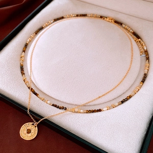Macro detail of gold plated compass necklace with brown gemstone and beaded chains