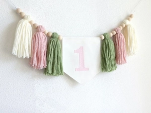 Detail of wooden beads with pink and green tassels and felt flag for first birthday decor