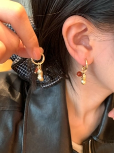 Gros plan d'une boucle d'oreille dorée en forme de cacahuète avec perle rouge