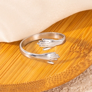 Macro shot of silver hug ring featuring hands embrace design on a soft satin background